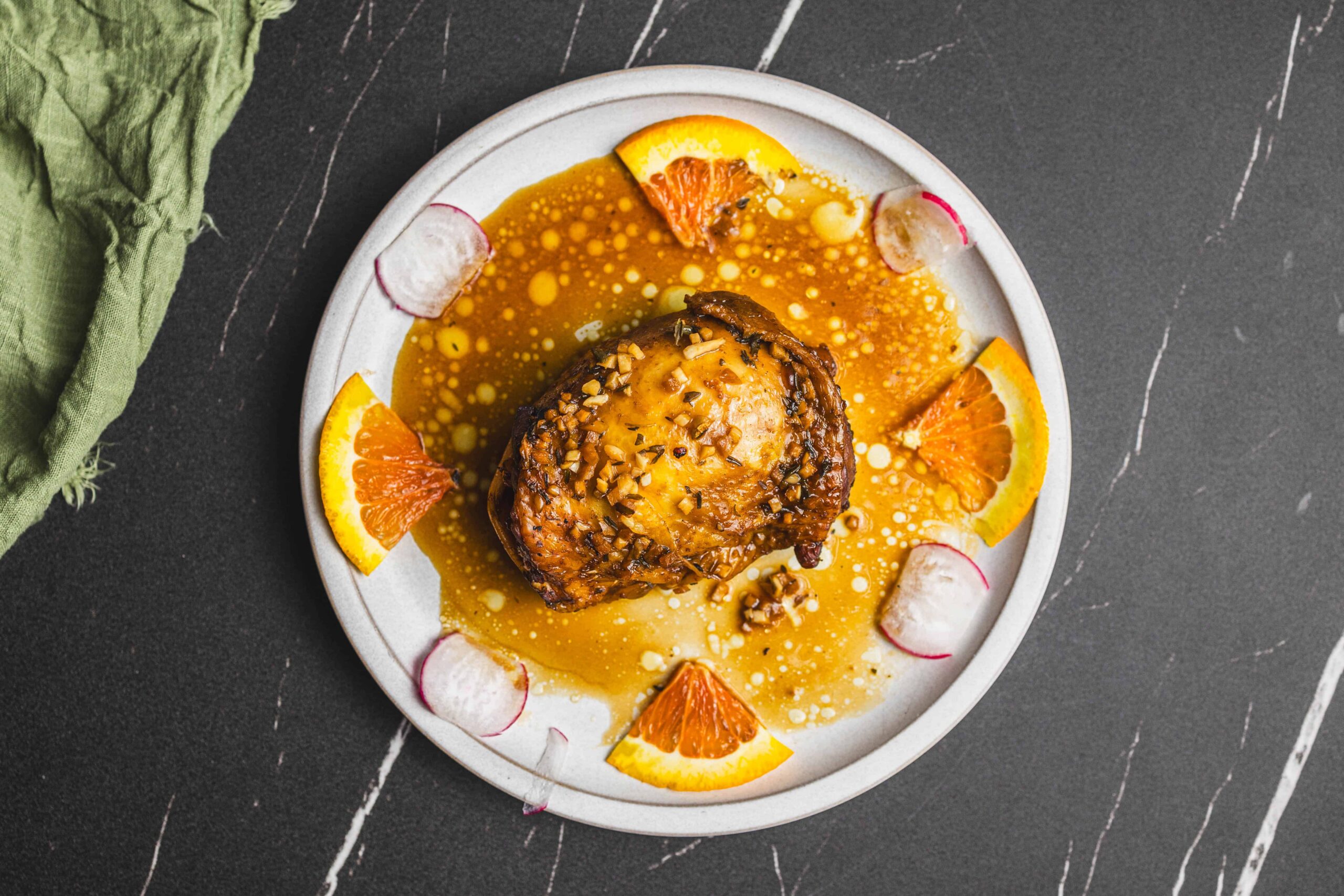 Roasted chicken with orange glaze and crunchy almond topping served with citrus slices and radish garnishes on a white plate. Perfect for flavorful dinner recipes and elegant plating.
