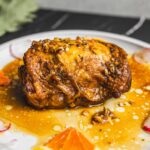 Succulent baked chicken thigh with caramelized sauce and chopped nuts garnished with fresh orange and radish slices on white plate, close-up, restaurant-quality food presentation, Hey Recipe.