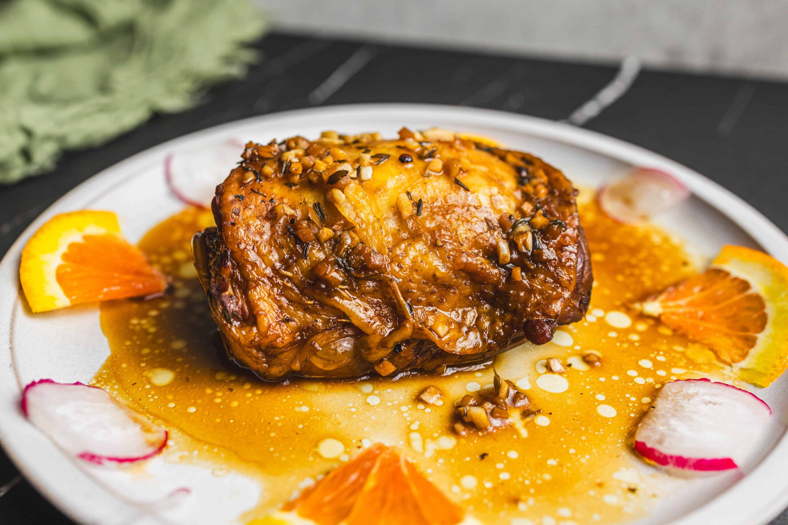 Succulent baked chicken thigh with caramelized sauce and chopped nuts garnished with fresh orange and radish slices on white plate, close-up, restaurant-quality food presentation, Hey Recipe.