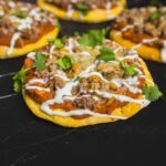 Savory beef and vegetable street tacos on corn tortillas topped with sour cream and fresh cilantro, served on a black wooden surface for vibrant presentation.