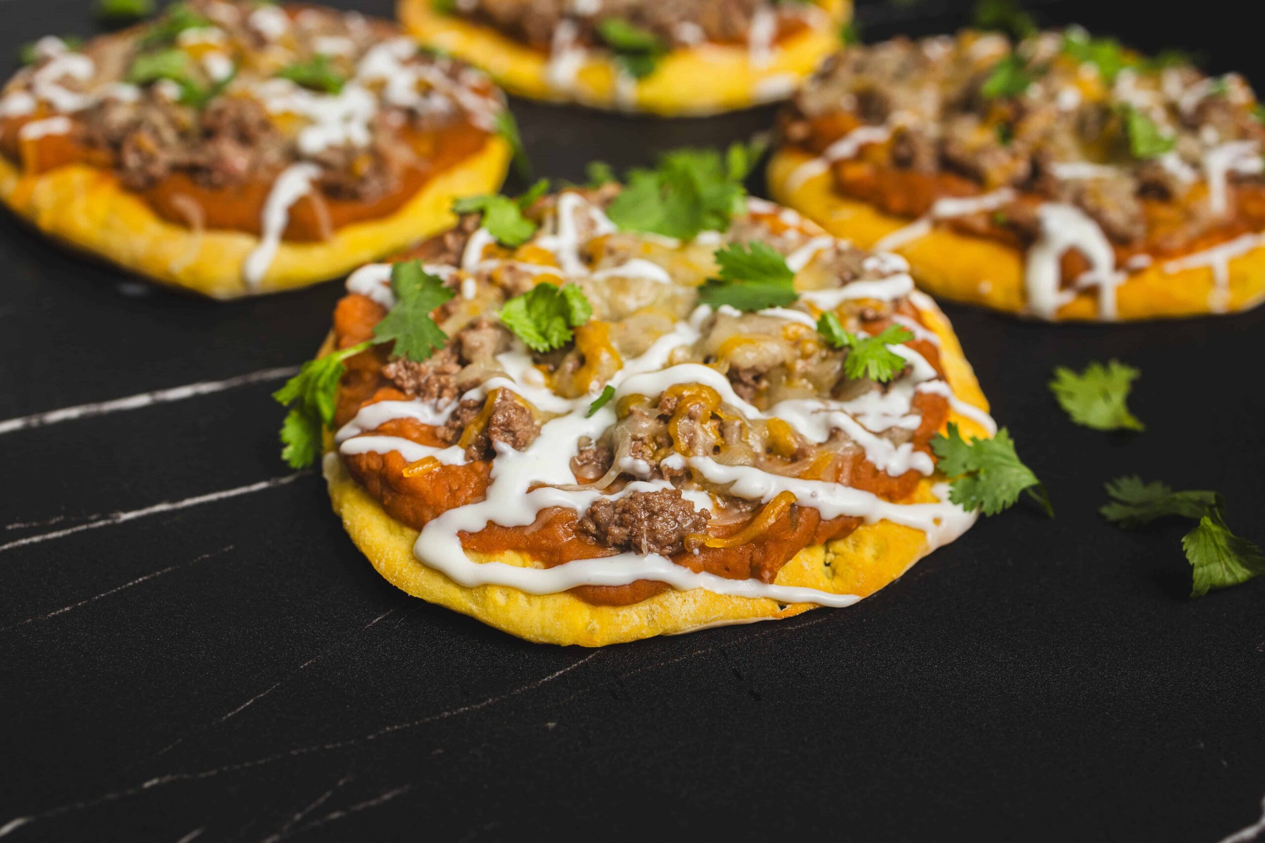 Savory beef and vegetable street tacos on corn tortillas topped with sour cream and fresh cilantro, served on a black wooden surface for vibrant presentation.