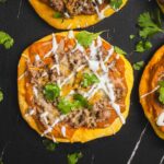 Savory taco stuffed sweet potatoes topped with seasoned ground beef, melted cheese, fresh cilantro, and drizzle of sour cream on black background for healthy comfort food recipes.