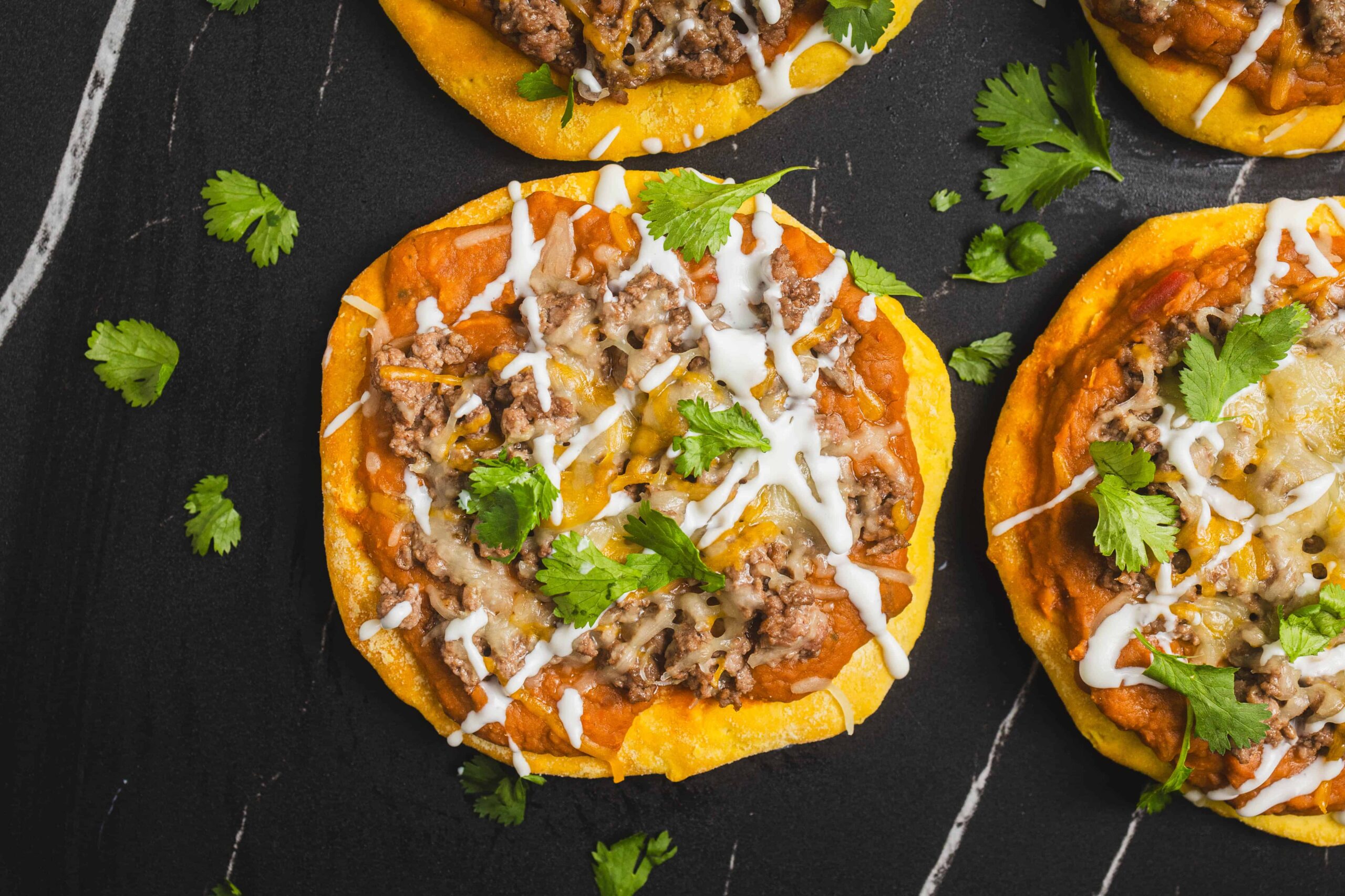Savory taco stuffed sweet potatoes topped with seasoned ground beef, melted cheese, fresh cilantro, and drizzle of sour cream on black background for healthy comfort food recipes.