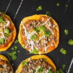 Flavorful mini taco pizzas topped with seasoned ground beef, melted cheese, fresh cilantro, and drizzled with sauce, served on a dark rustic surface for an easy and delicious appetizer or snack.