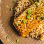 Juicy pan-seared salmon with crispy skin served over fluffy brown rice, garnished with chopped green onions on a rustic plate for a healthy, delicious seafood meal.