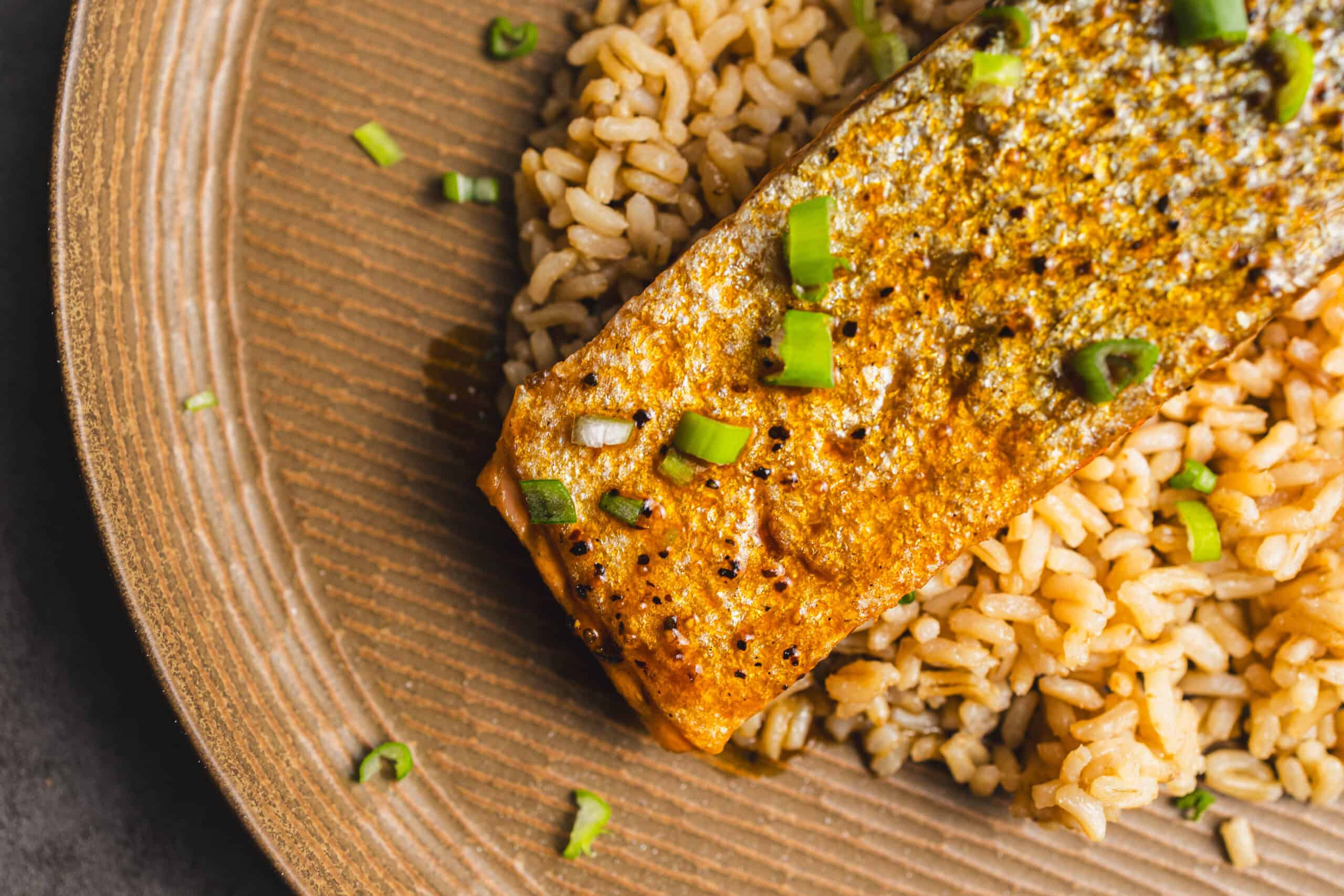 Juicy pan-seared salmon with crispy skin served over fluffy brown rice, garnished with chopped green onions on a rustic plate for a healthy, delicious seafood meal.
