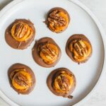 Decadent chocolate caramel pecan cups arranged on a white plate, featuring rich chocolate coating, caramel drizzle, and crunchy pecans for a delicious dessert treat.