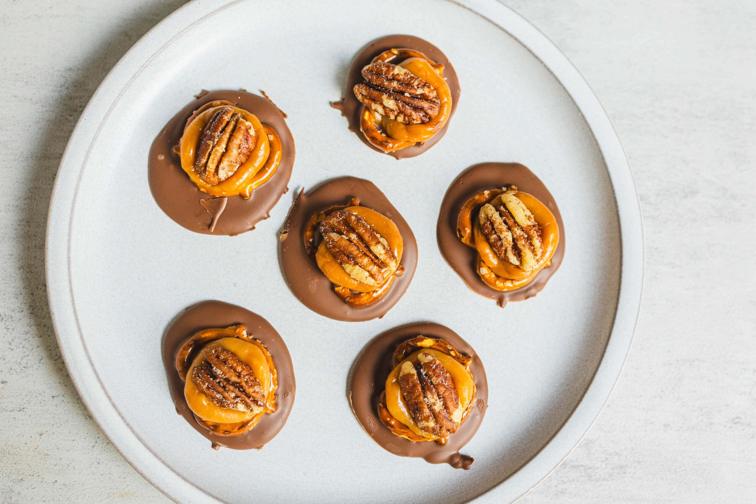 Decadent chocolate caramel pecan cups arranged on a white plate, featuring rich chocolate coating, caramel drizzle, and crunchy pecans for a delicious dessert treat.
