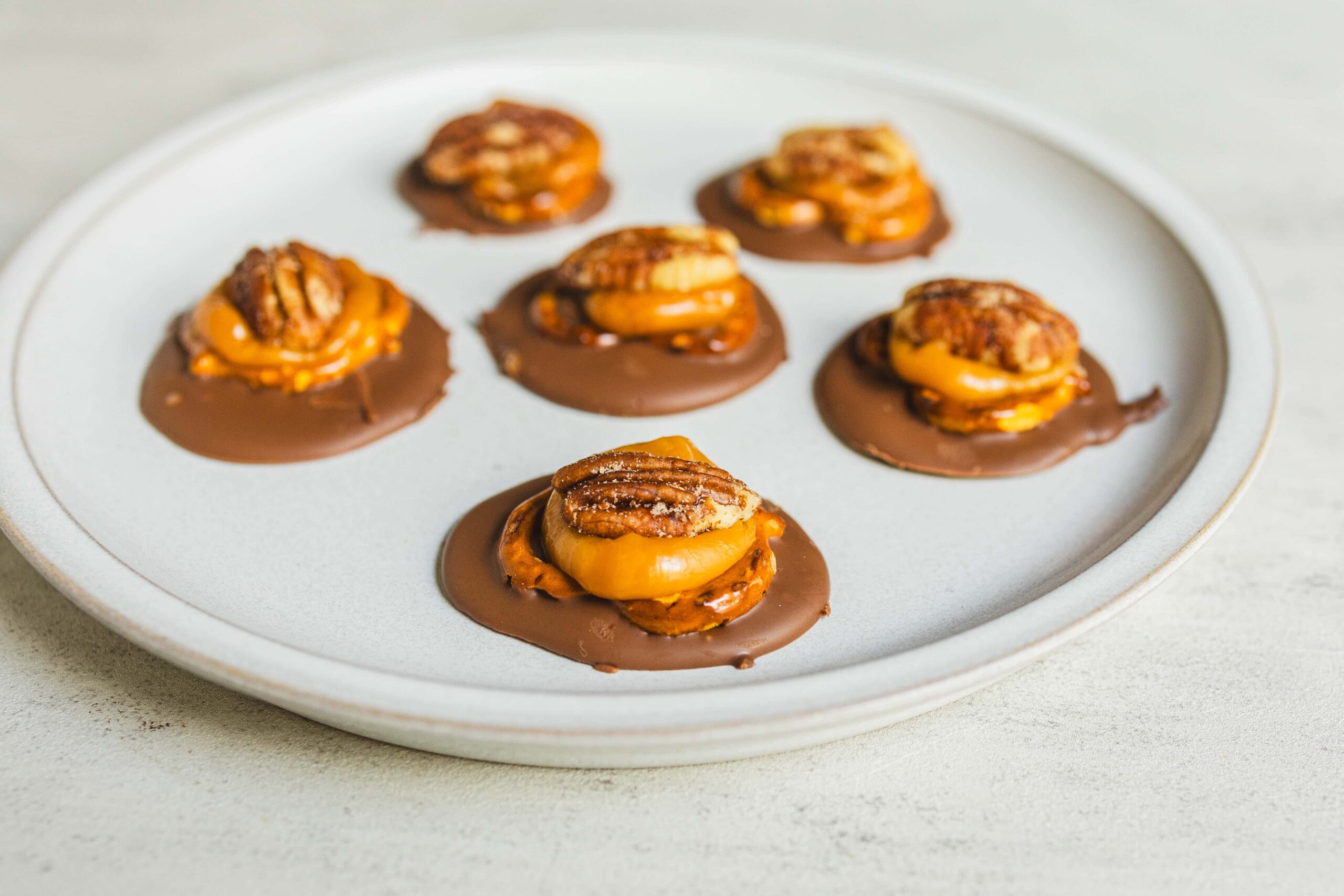 Peanut butter cup pretzel bites with caramel and pecans on a white plate, perfect for snack recipes and quick desserts.