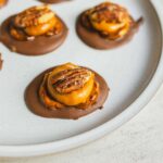 Rich chocolate-dipped cookies topped with caramelized banana slices and pecans, served on a white platter, perfect for decadent dessert recipes and sweet treat indulgence.