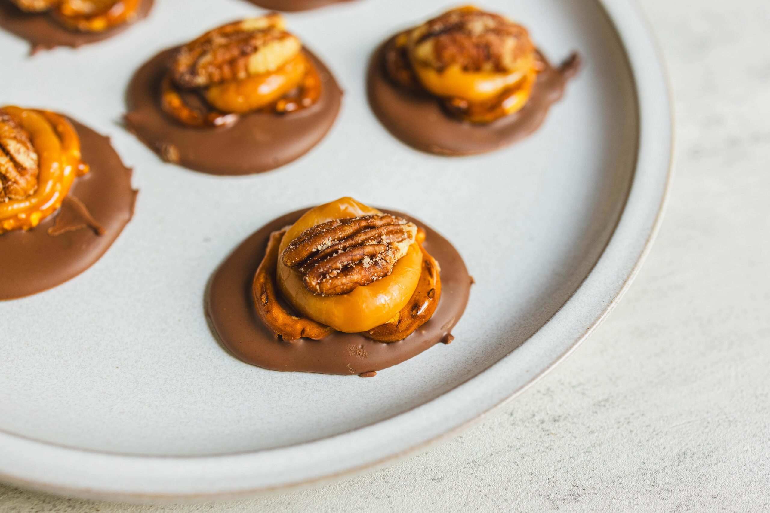 Rich chocolate-dipped cookies topped with caramelized banana slices and pecans, served on a white platter, perfect for decadent dessert recipes and sweet treat indulgence.