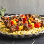 Juicy beef and vegetable skewers on a bed of cooked orzo pasta, served on a rustic ceramic plate, perfect for grilling and summer barbecues.