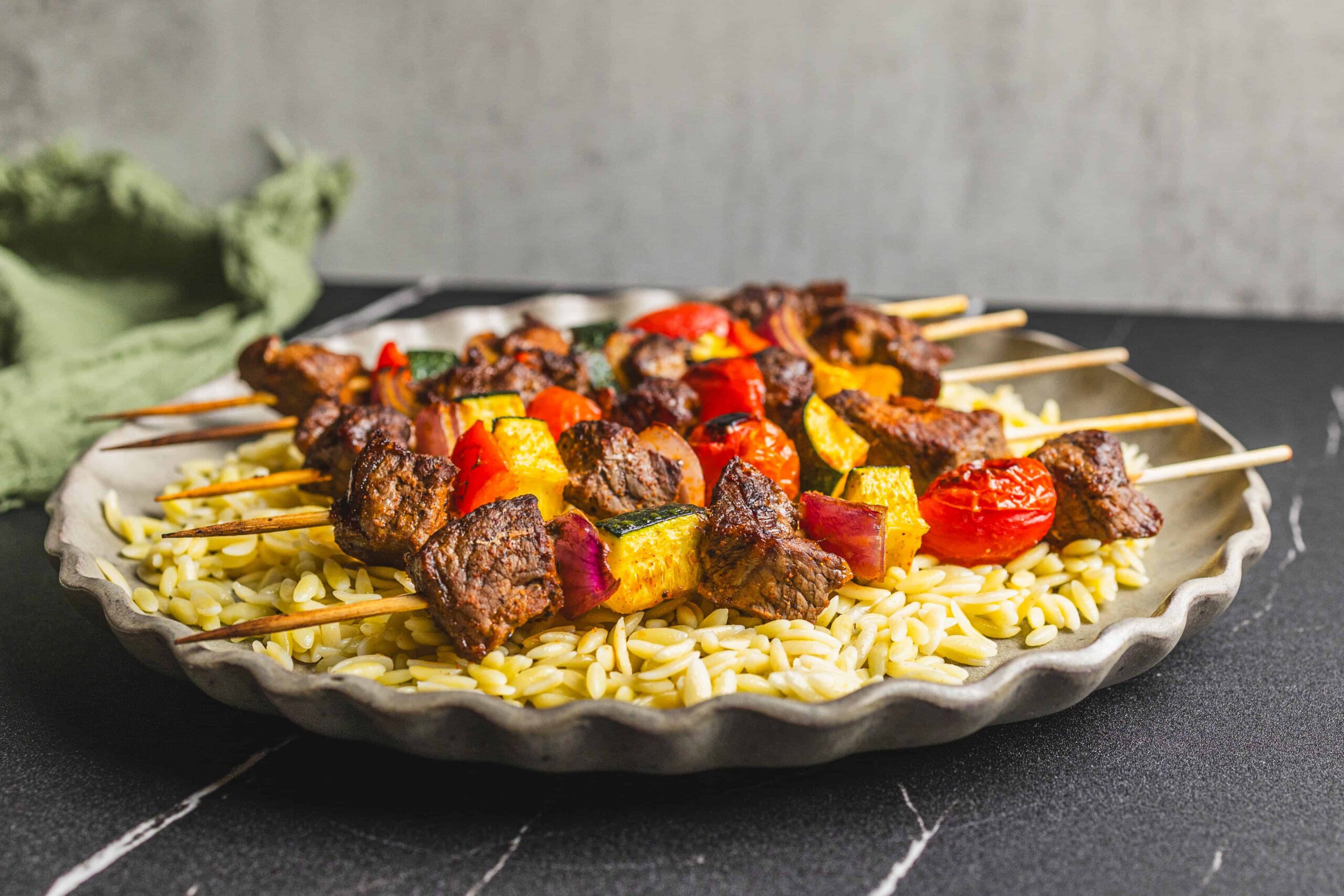 Juicy beef and vegetable skewers on a bed of cooked orzo pasta, served on a rustic ceramic plate, perfect for grilling and summer barbecues.
