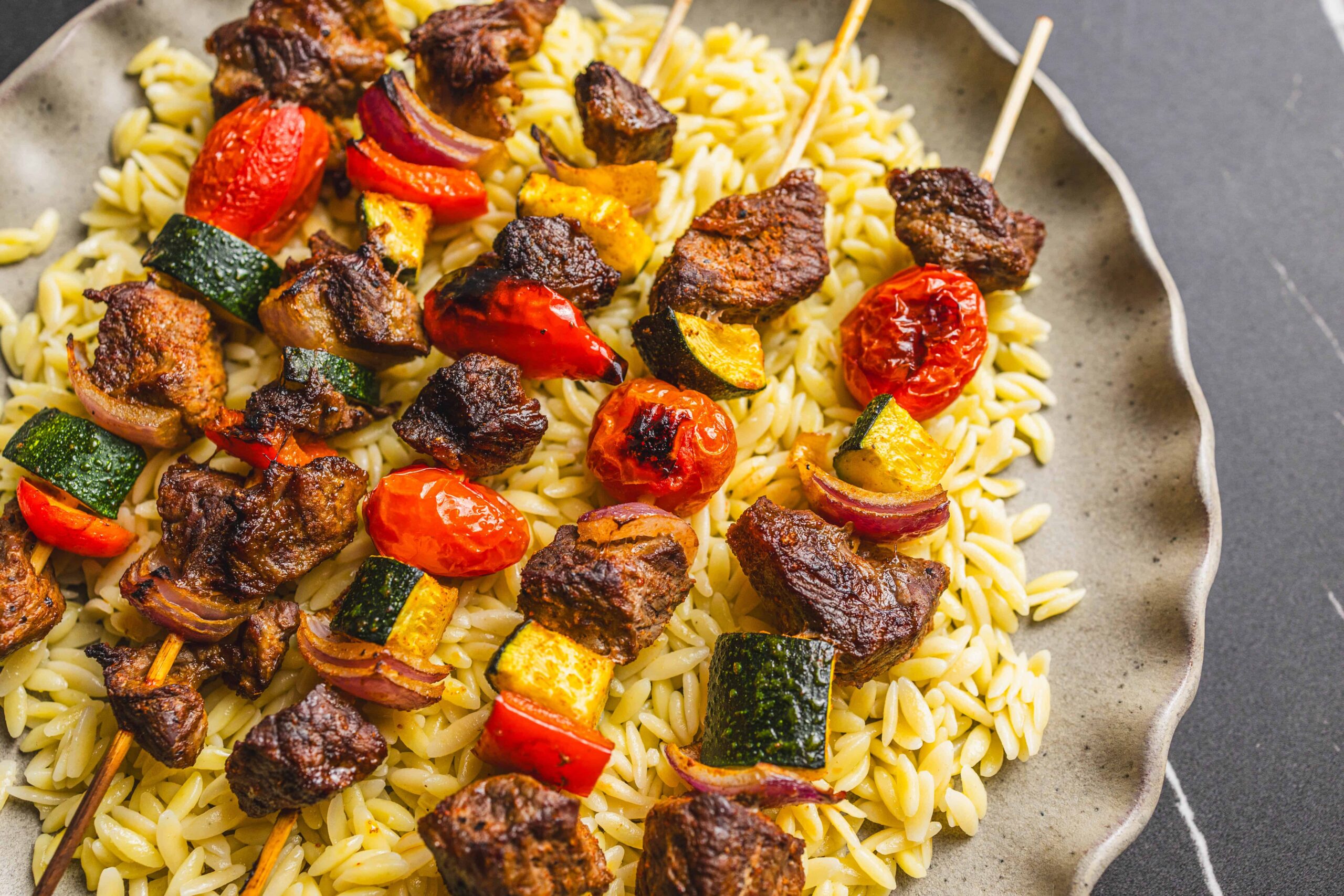 Juicy beef and vegetable skewers served over orzo pasta, flavorful grilled meat, colorful grilled vegetables, perfect for easy delicious summer recipes, healthy dinner ideas, and barbecue meals.