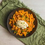 Creamy tomato sauce fusilli pasta topped with grated cheese and fresh herbs in a black bowl on a rustic green cloth.