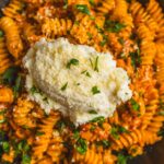 Creamy mashed potatoes atop flavorful spaghetti with tomato sauce, garnished with fresh chopped parsley, served on a black plate for a delicious comfort food meal.