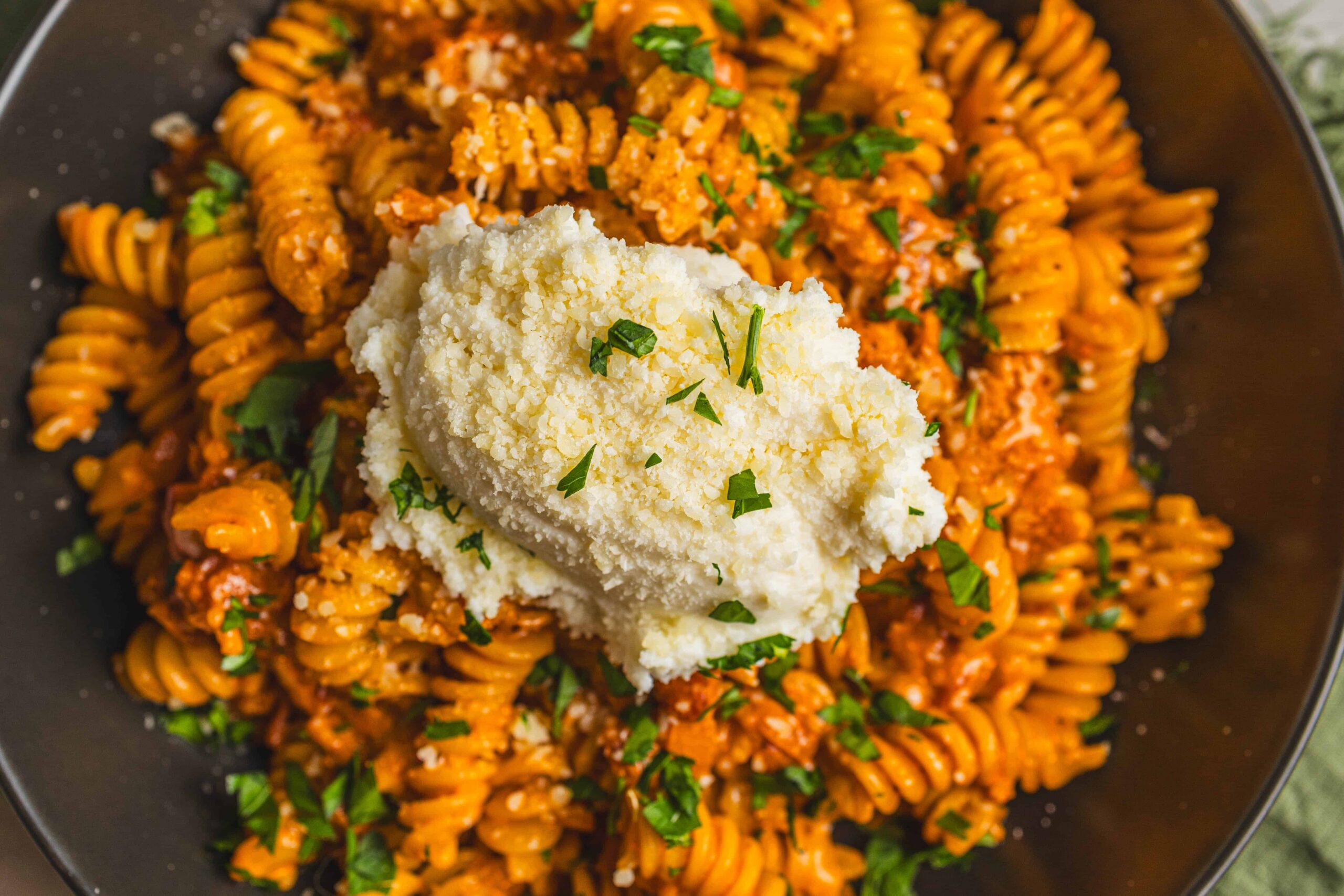 Creamy mashed potatoes atop flavorful spaghetti with tomato sauce, garnished with fresh chopped parsley, served on a black plate for a delicious comfort food meal.