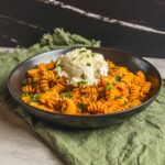 Creamy tomato pasta fusilli with basil and a dollop of ricotta cheese on top, served in a black bowl on a rustic table with green cloth. Perfect comfort food for pasta lovers.