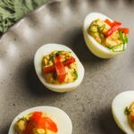 Savory stuffed eggs with red bell peppers and green onions on a rustic gray plate.