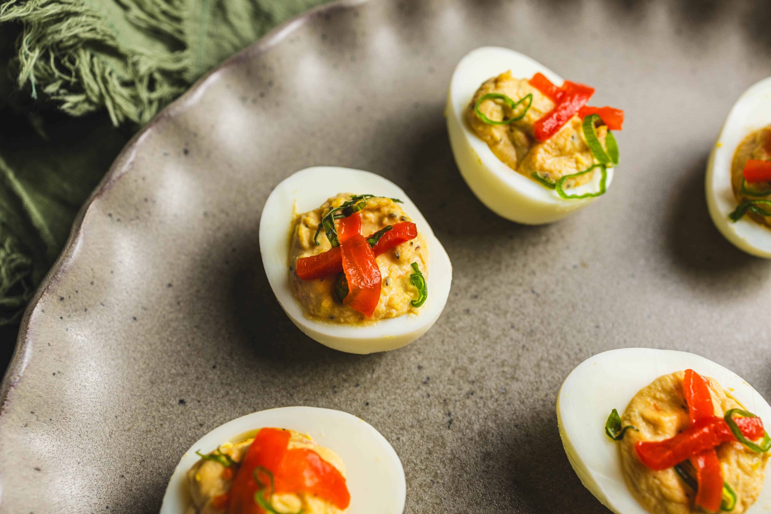 Savory stuffed eggs with red bell peppers and green onions on a rustic gray plate.