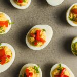 Boiled eggs stuffed with creamy filling, topped with chopped red bell peppers and green onions, served as a delicious appetizer or party snack.