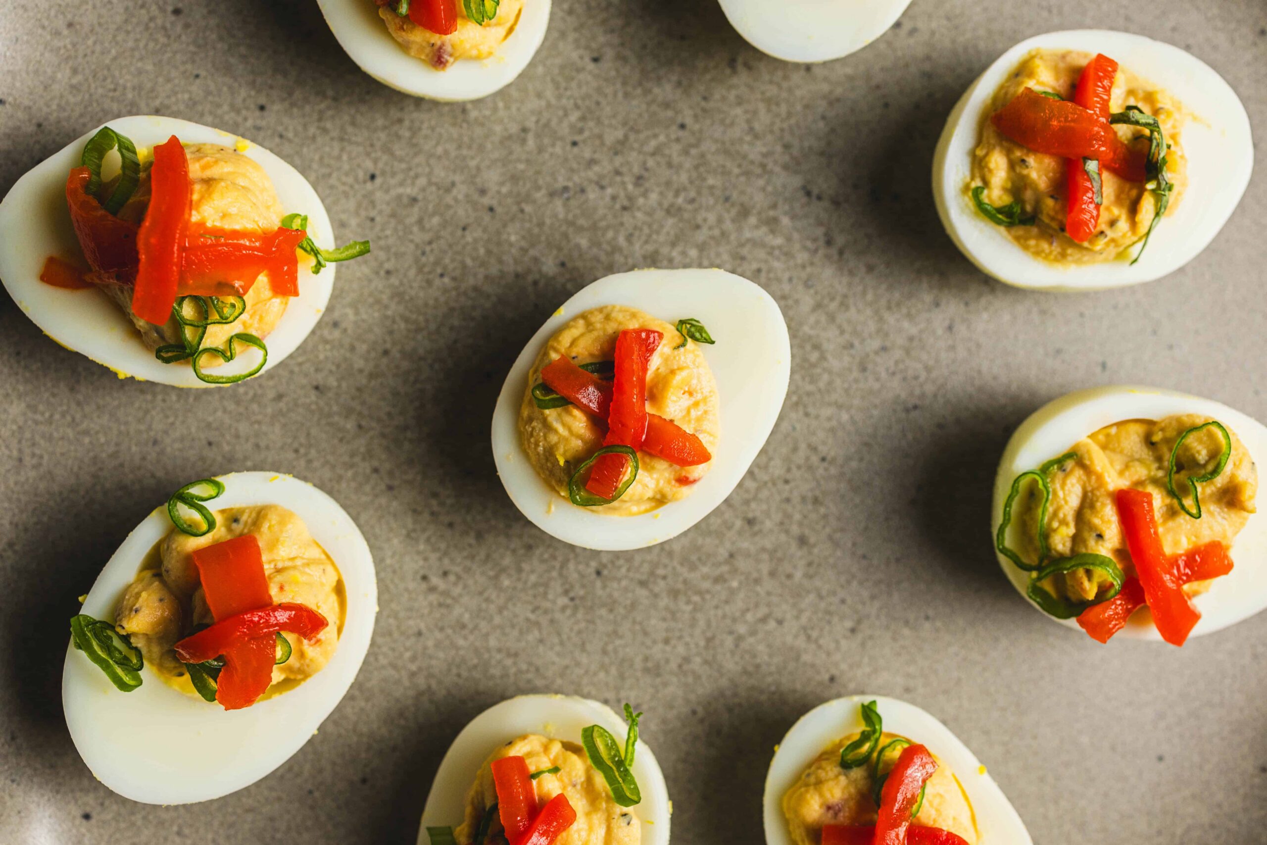 Boiled eggs stuffed with creamy filling, topped with chopped red bell peppers and green onions, served as a delicious appetizer or party snack.