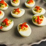 Boiled eggs stuffed with seasoned egg yolk and topped with chopped red and green bell peppers, ready to serve as a nutritious appetizer or snack.