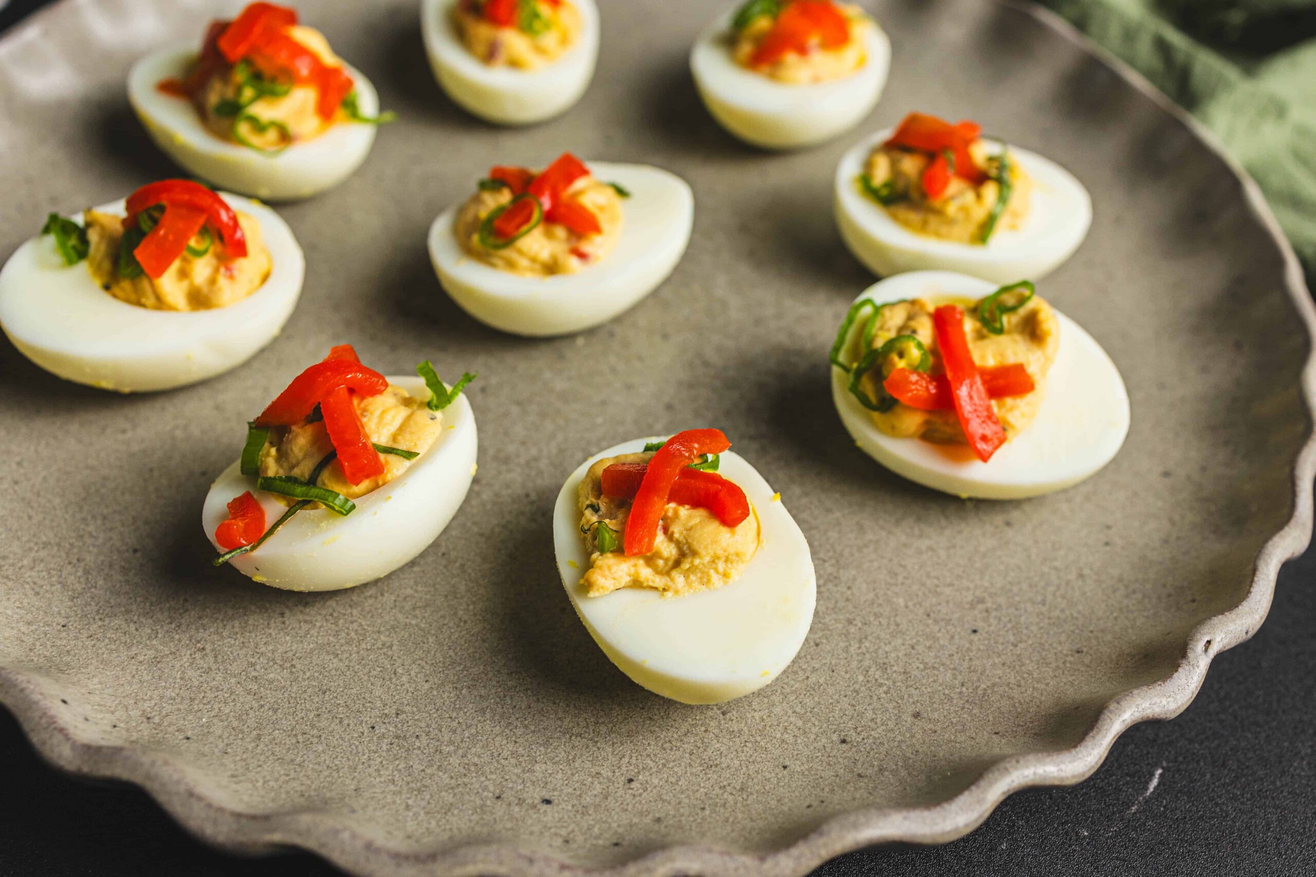 Boiled eggs stuffed with seasoned egg yolk and topped with chopped red and green bell peppers, ready to serve as a nutritious appetizer or snack.