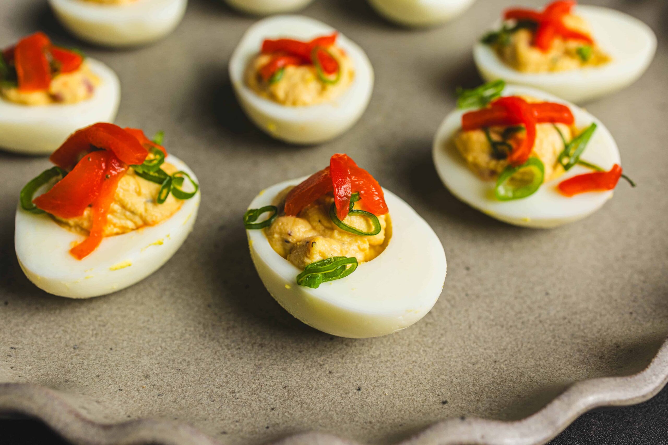 Hard-boiled eggs stuffed with savory filling, topped with red bell peppers and green onions, served as a delicious appetizer or party snack. Perfect for keto, low-carb diets, or finger foods.