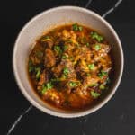 Savory beef chili in a white bowl garnished with fresh cilantro on a dark marble surface.