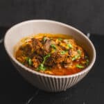 Slow-cooked beef stew in a rustic white bowl, garnished with fresh cilantro, served with rich, savory gravy, perfect for comforting home-cooked meals.