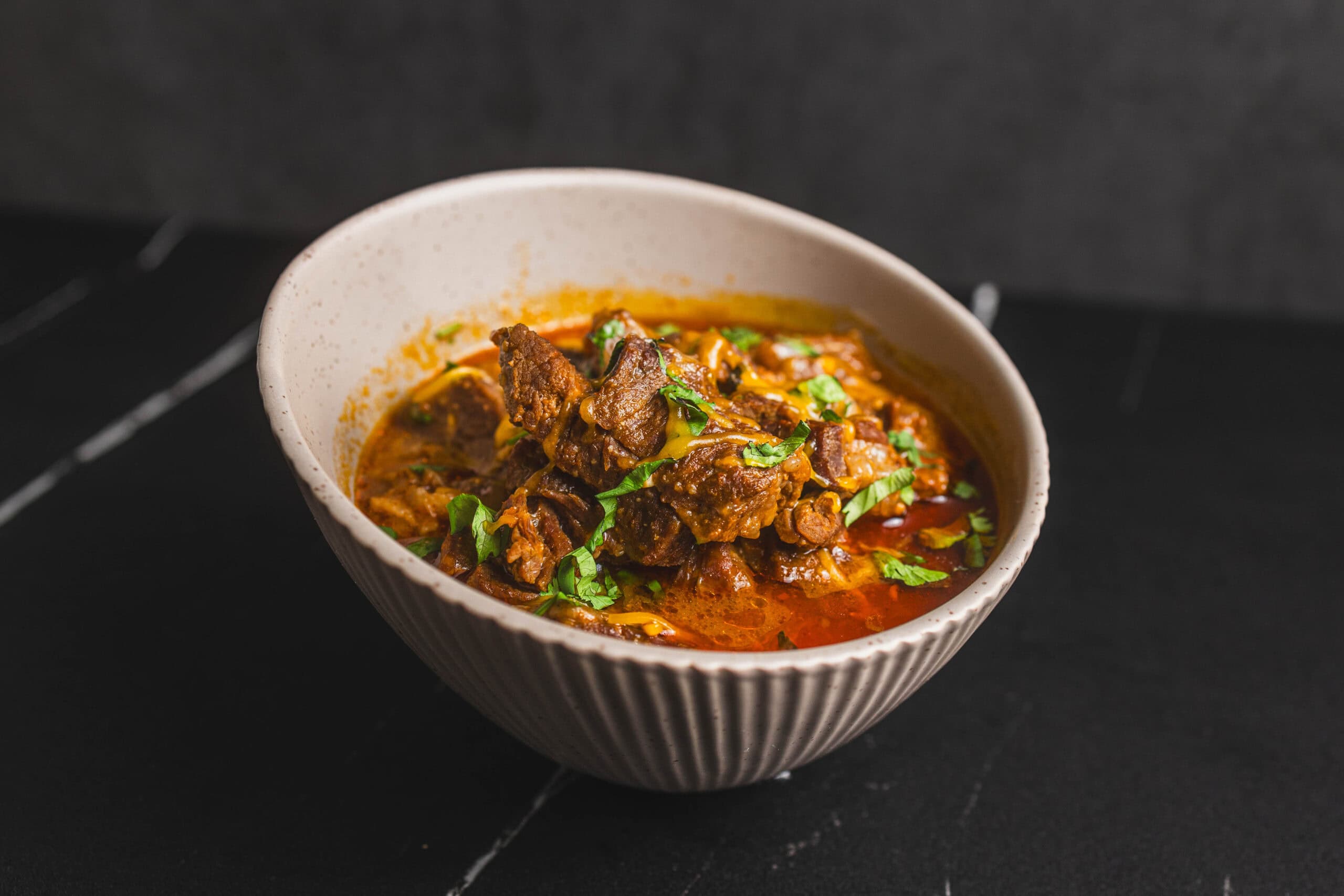 Slow-cooked beef stew in a rustic white bowl, garnished with fresh cilantro, served with rich, savory gravy, perfect for comforting home-cooked meals.