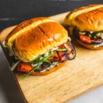 Grilled vegetable banh mi sandwiches with roasted peppers, fresh herbs, and toasted baguette on wooden board. Perfect for vegan or vegetarian meal options.