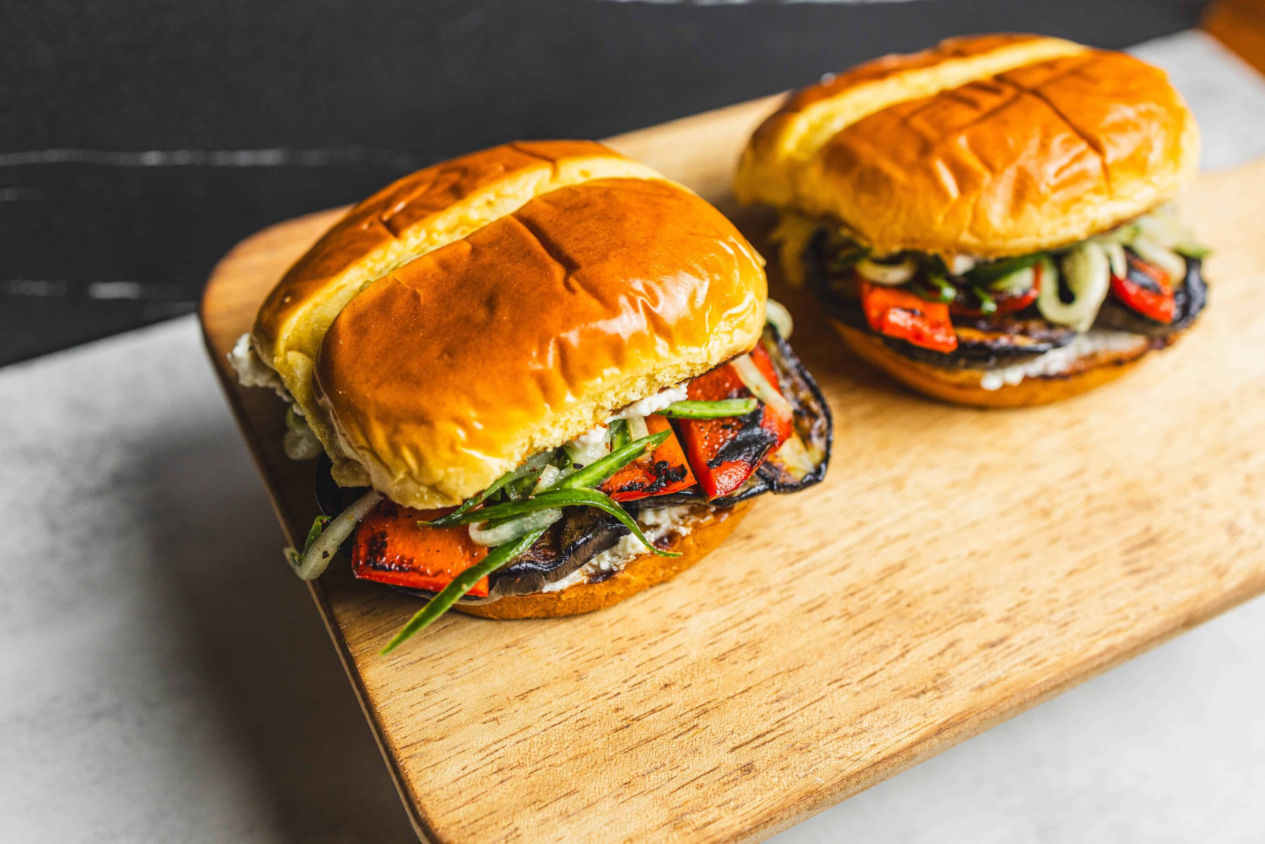 Grilled vegetable banh mi sandwiches with roasted peppers, fresh herbs, and toasted baguette on wooden board. Perfect for vegan or vegetarian meal options.