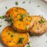 Sweet roasted sweet potatoes garnished with chopped cilantro on a rustic ceramic plate, perfect for healthy vegetarian meals or side dishes.