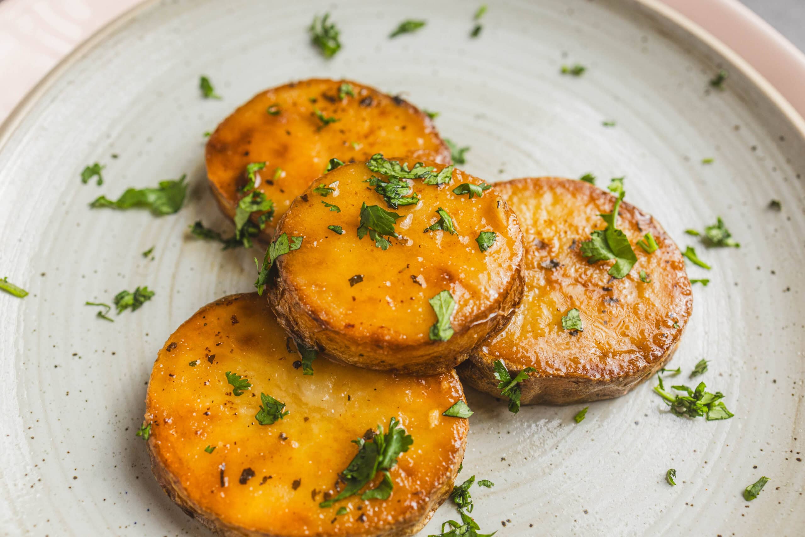 Sweet roasted sweet potatoes garnished with chopped cilantro on a rustic ceramic plate, perfect for healthy vegetarian meals or side dishes.