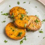 Golden roasted sweet potatoes topped with fresh herbs and black pepper, served on a stylish ceramic plate. Perfect for healthy recipes, side dishes, and nutritious meal ideas.