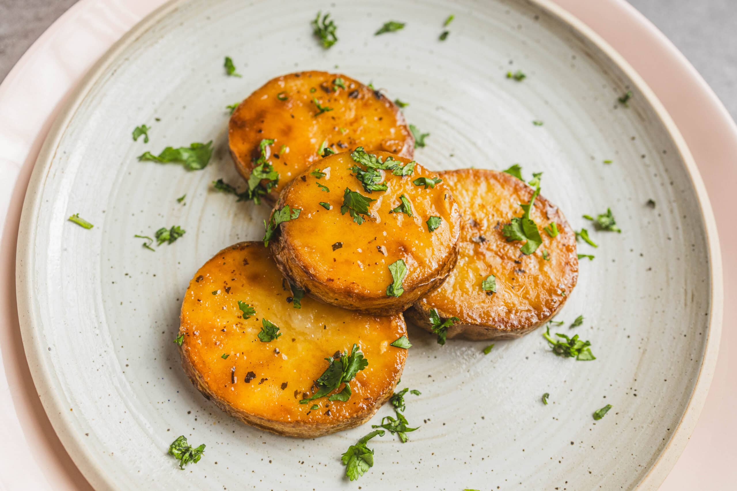 Golden roasted sweet potatoes topped with fresh herbs and black pepper, served on a stylish ceramic plate. Perfect for healthy recipes, side dishes, and nutritious meal ideas.