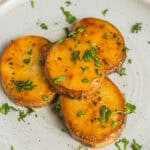 Roasted sweet potatoes with herbs on a ceramic plate.