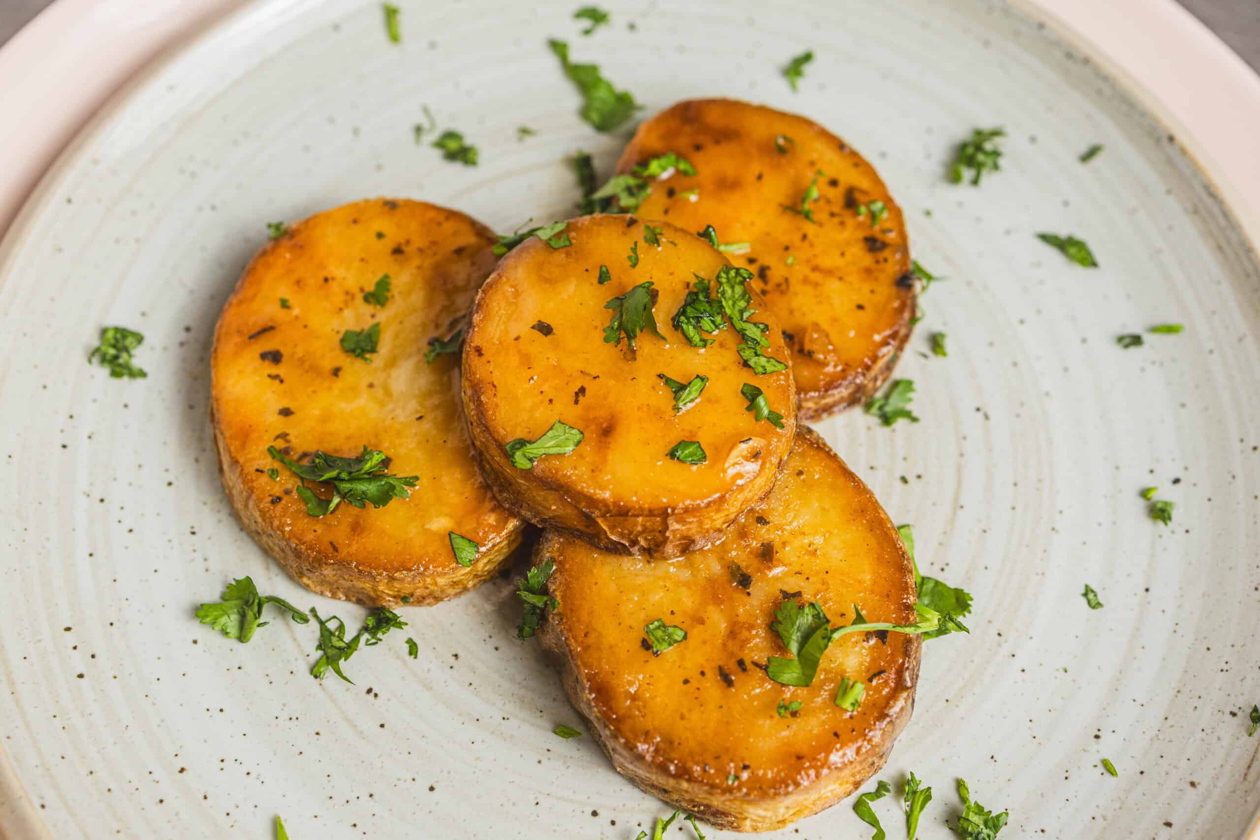 Roasted sweet potatoes with herbs on a ceramic plate.