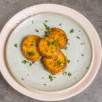 Roasted sweet potato slices garnished with fresh chopped parsley on a ceramic plate.