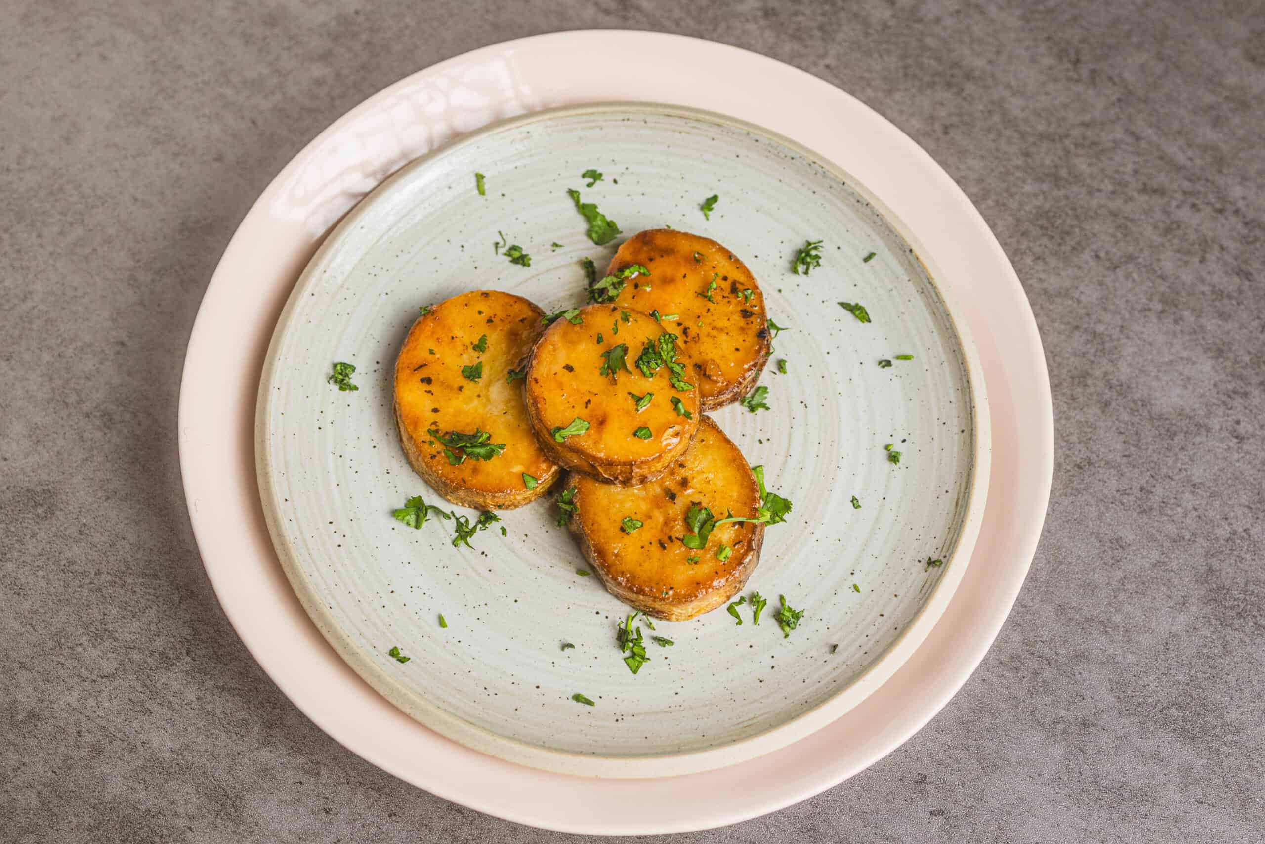 Roasted sweet potato slices garnished with fresh chopped parsley on a ceramic plate.