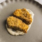 Crispy breaded chicken fillets served on a bed of creamy white sauce on a rustic gray plate. Perfectly golden and crunchy, ideal for a delicious homemade dinner or appetizer.