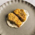 Crispy breaded chicken tenders served over creamy herb sauce on a rustic beige plate. Perfect for easy dinner recipes and comfort food.