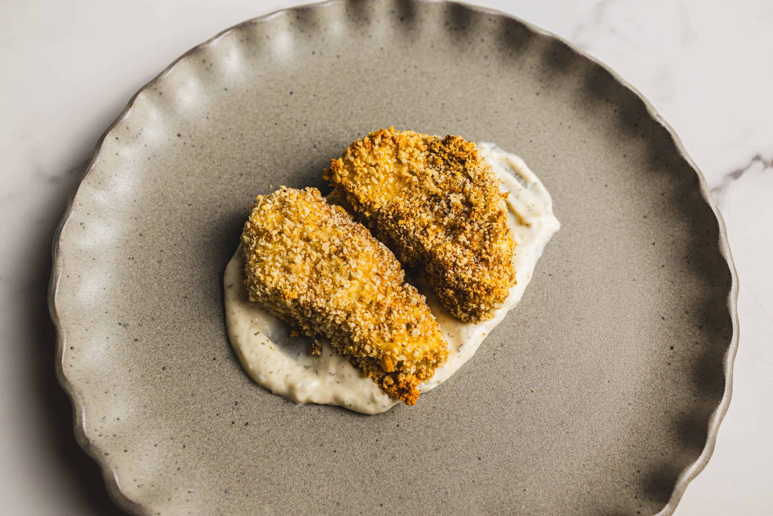 Crispy breaded chicken tenders served over creamy herb sauce on a rustic beige plate. Perfect for easy dinner recipes and comfort food.