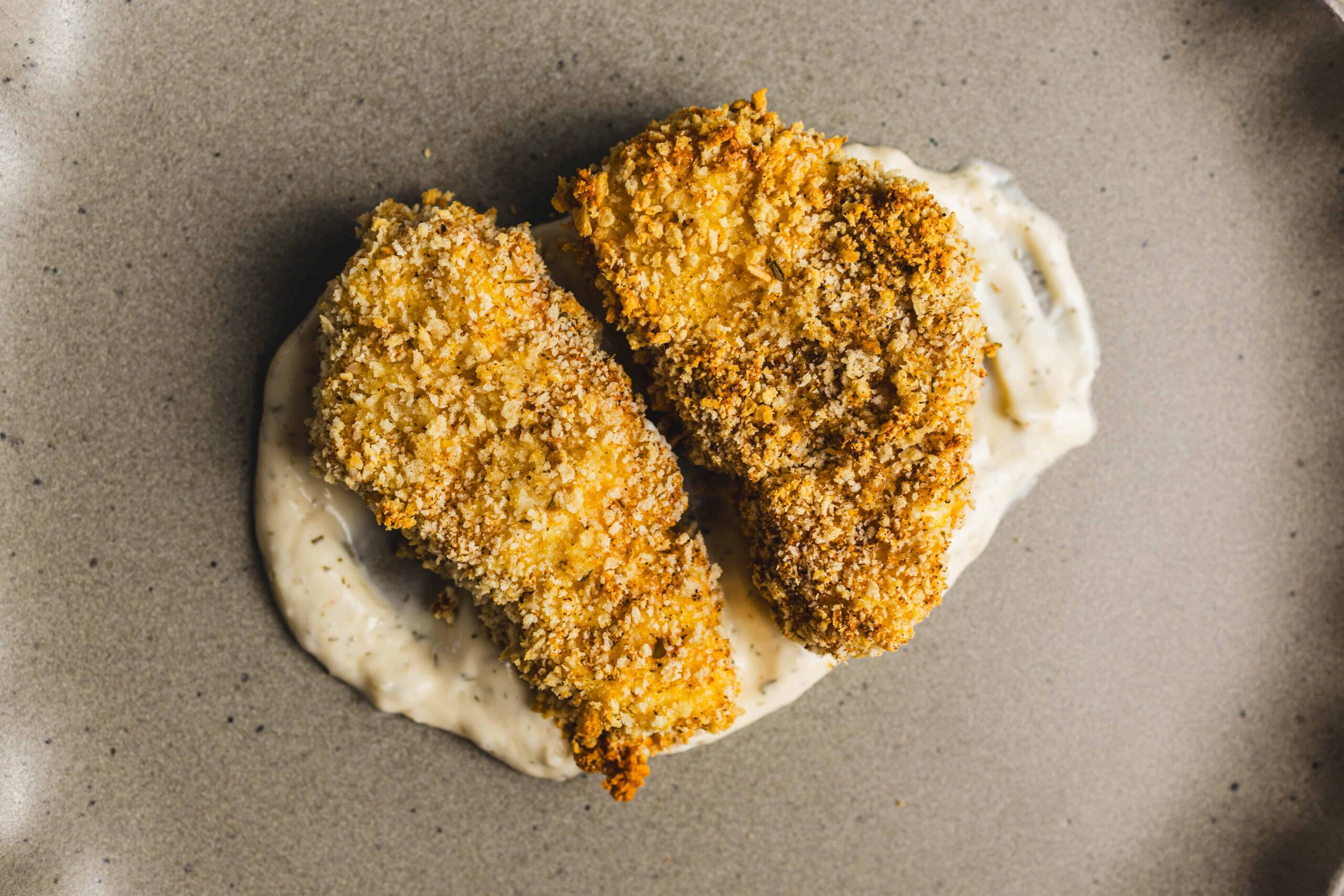 Crispy breaded fried chicken tenders on a bed of creamy dipping sauce, served on a neutral-colored plate, highlighting delicious American comfort food.
