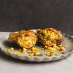 Baked chicken breast stuffed with corn, cheese, and herbs on a rustic plate, served as a savory and flavorful comfort food dish.