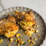 Juicy baked chicken breasts stuffed with corn and cheese, seasoned with herbs, served on a rustic gray plate for a flavorful and comforting meal.