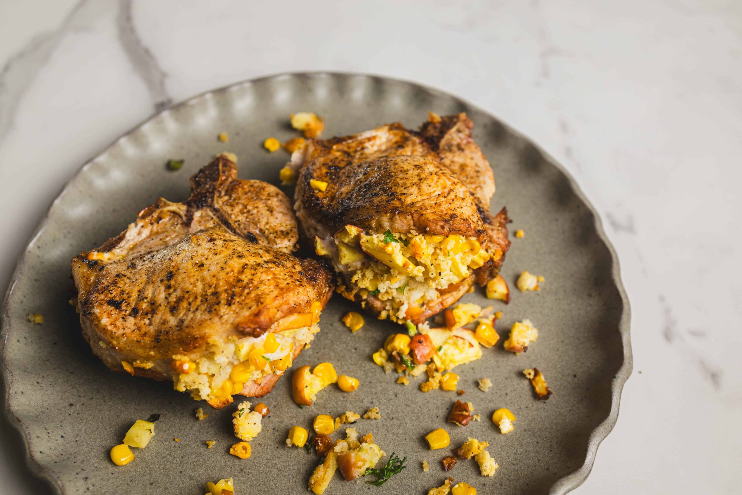 Juicy baked chicken breasts stuffed with corn and cheese, seasoned with herbs, served on a rustic gray plate for a flavorful and comforting meal.
