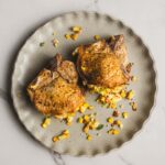 Juicy baked chicken thighs served with a fresh vegetable and corn stuffing, garnished with chopped herbs on a rustic ceramic plate. Perfect for a flavorful and hearty meal.